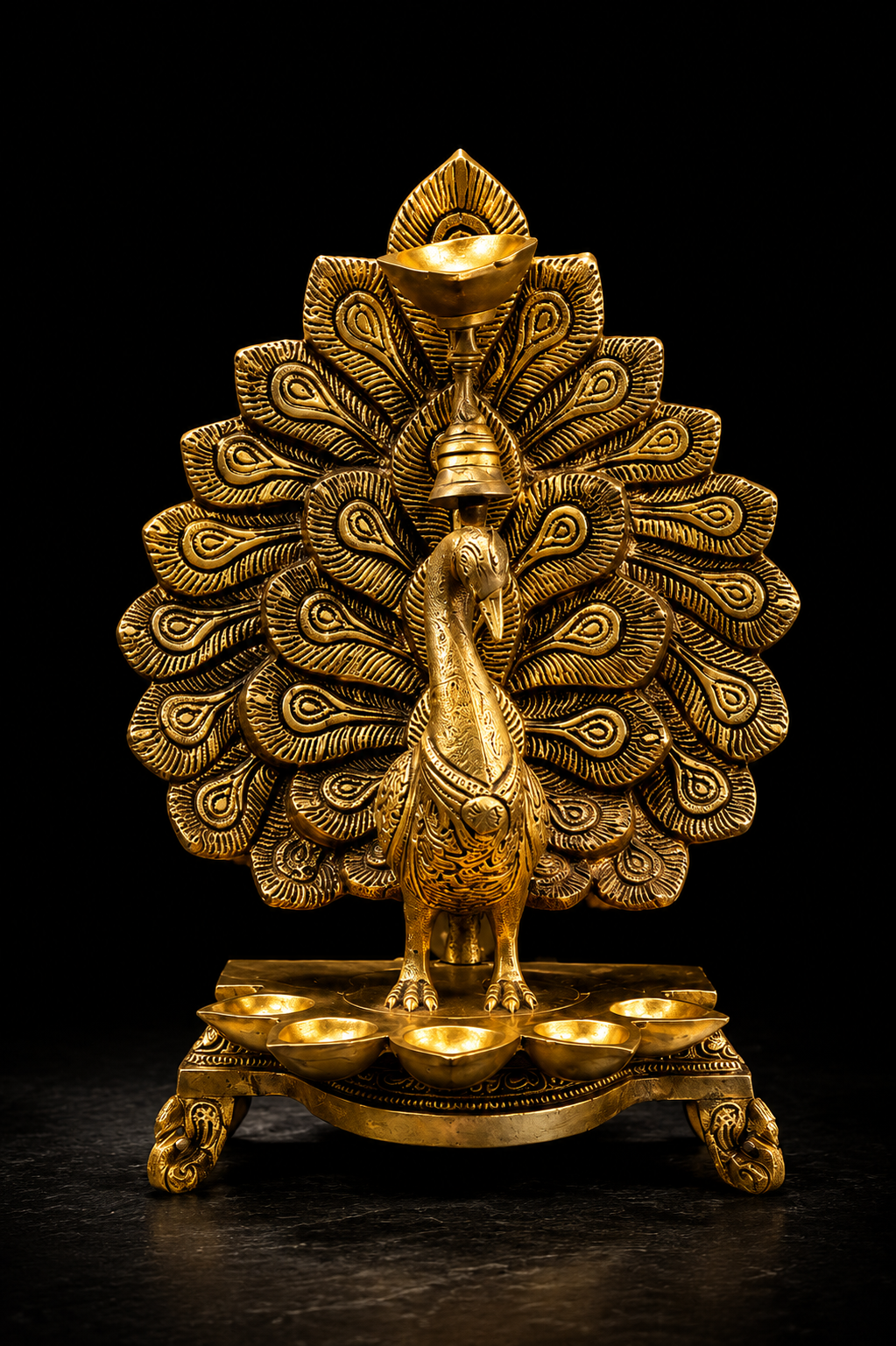 A golden peacock figurine with a large fanned tail and a small base of oil lamps, photographed against a solid black background.
